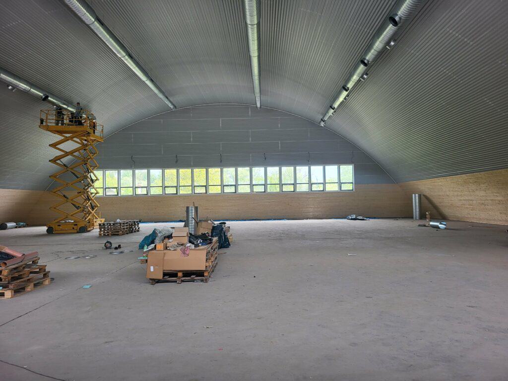 Interiér nové tenisové haly ve Vranově nad Topľou během výstavby – oblouková konstrukce, instalace vzduchotechniky a příprava na povrch kurtů.