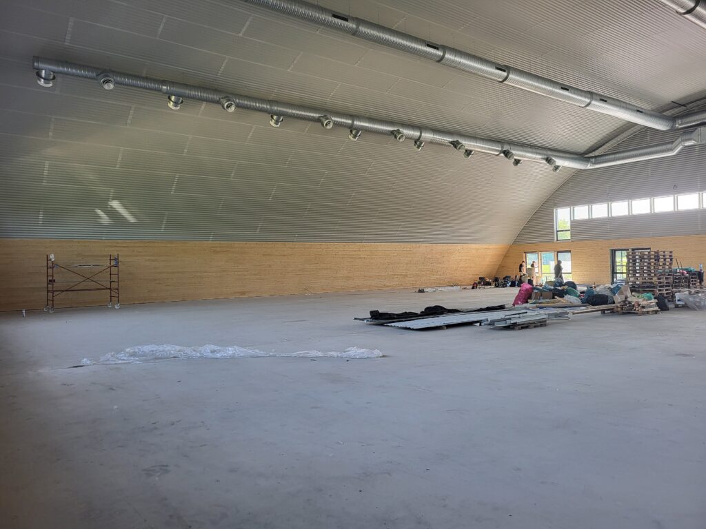 Interiér obloukové montované ocelové haly HUPRO v průběhu dokončovacích prací, s výrazným bezsloupovým prostorem a ventilačními vzduchotechnickými rozvody.