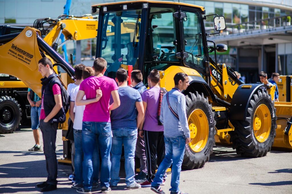 Návštěvníci veletrhu SEEBBE sledují prezentaci stavební techniky a žlutého kolového nakladače ve venkovní expozici Belgrade Fair.