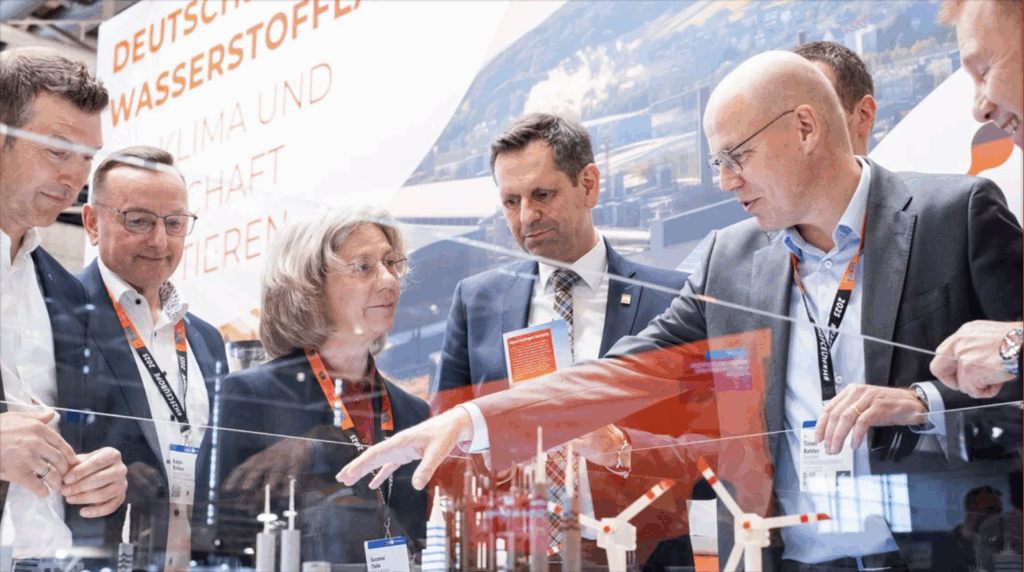 Odborní návštěvníci na Hannover Messe diskutují o technologiích a energetických řešeních u modelu větrné infrastruktury.