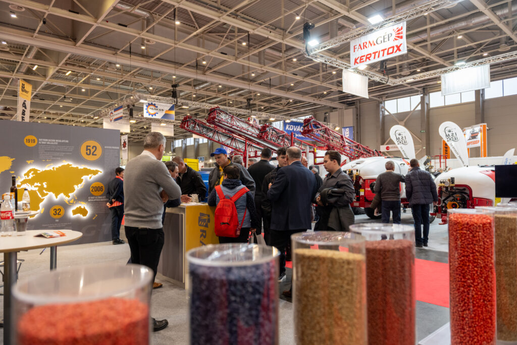 Návštěvníci na stáncích výrobců zemědělské techniky na AGROMASH Expo, s prezentacemi postřikovačů, osiv a firem jako FarmGép či Kertitox.