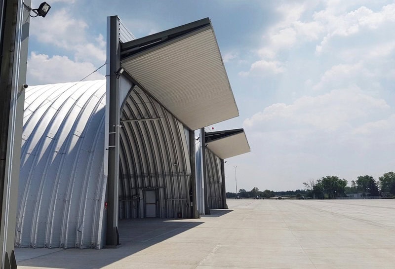 Obloukový ocelový letecký hangár s výklopnými hangárovými vraty od HUPRO SYSTEMS SE