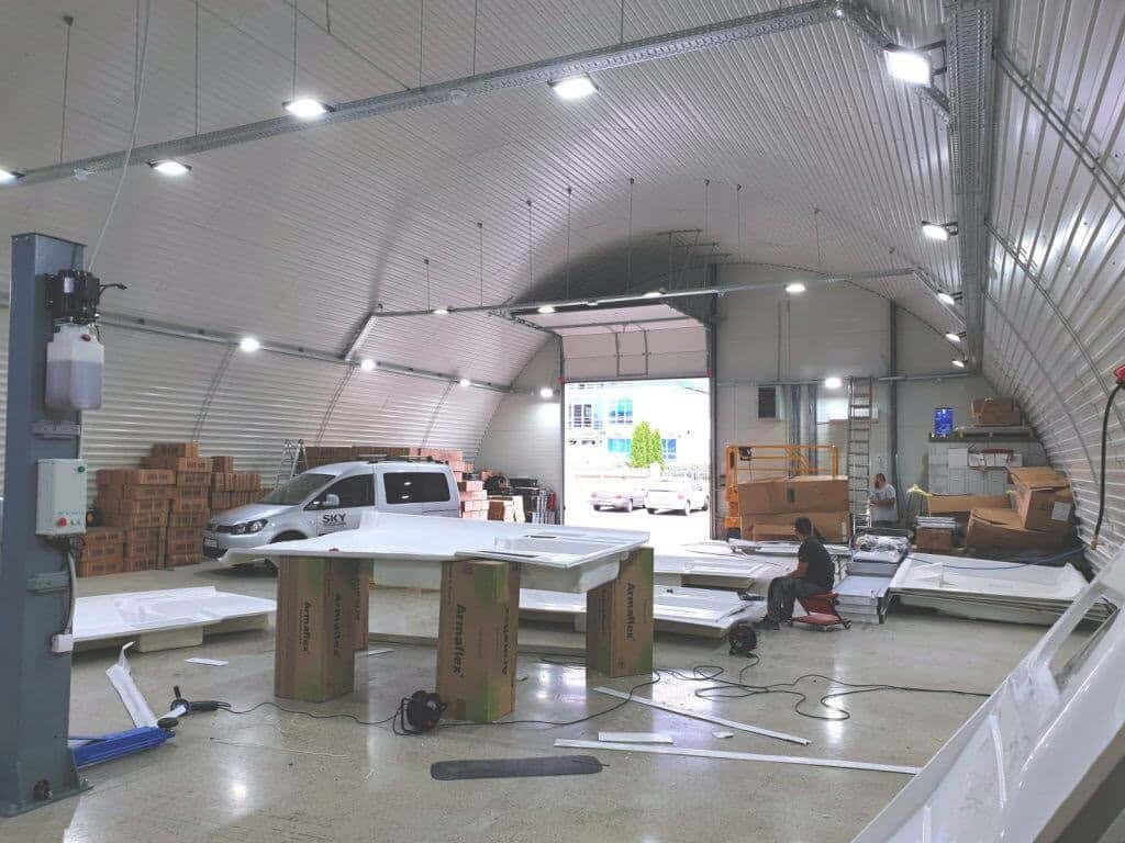 Interiér obloukové ocelové haly – průmyslová dílna a sklad s montážními pracemi, vozidlem a uloženým materiálem v moderní samonosné hale HUPRO SYSTEMS SE